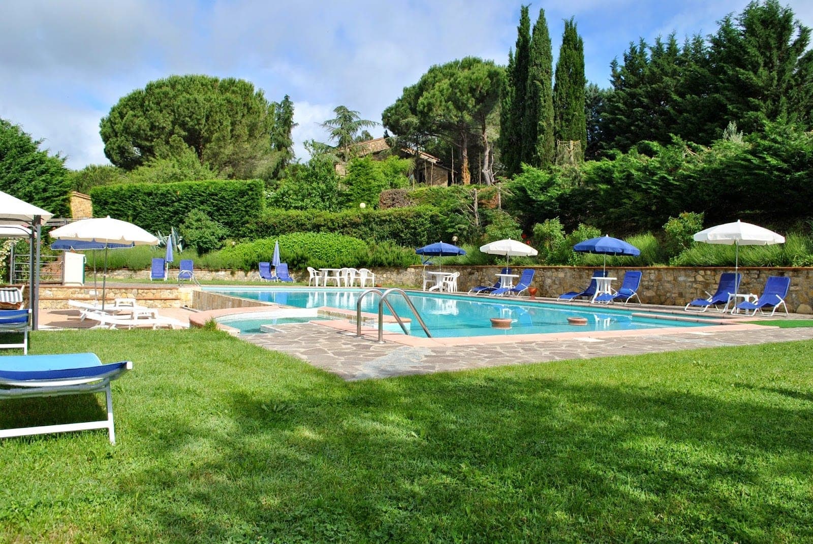Swimming pool with lounge chairs and umbrellas surrounded by greenery.