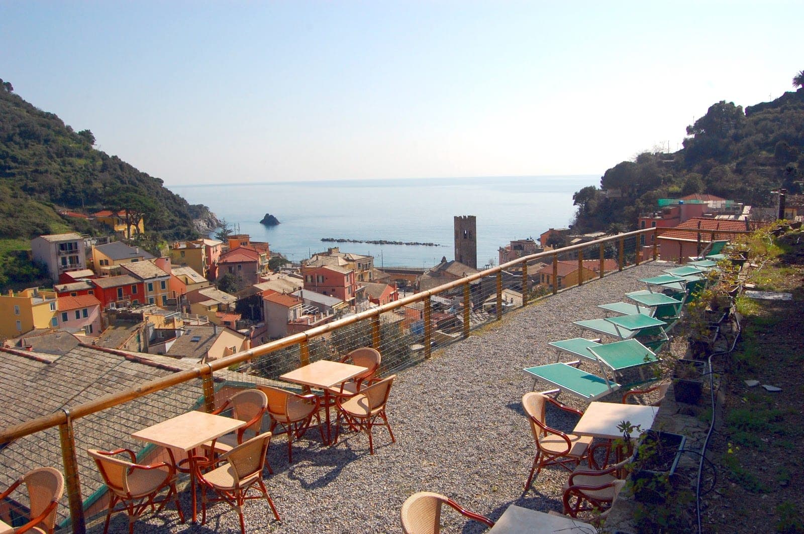 Terrace with tables and chairs overlooking a coastal town and the sea.