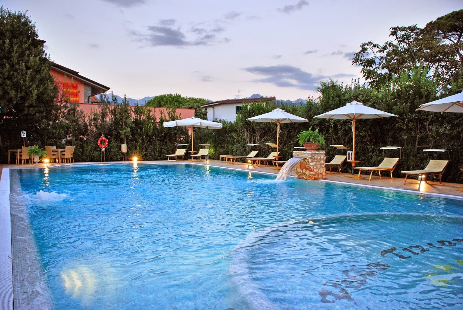 Swimming pool with lounge chairs and umbrellas at dusk.