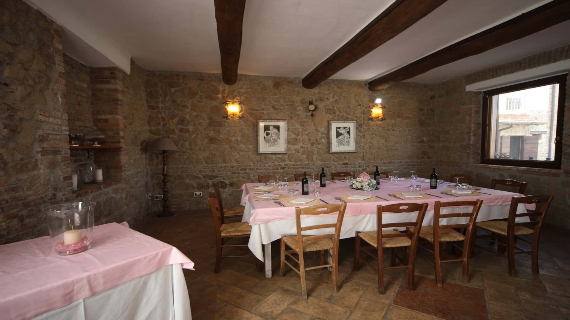 A long dining table covered with a pink tablecloth is set for a wedding reception.