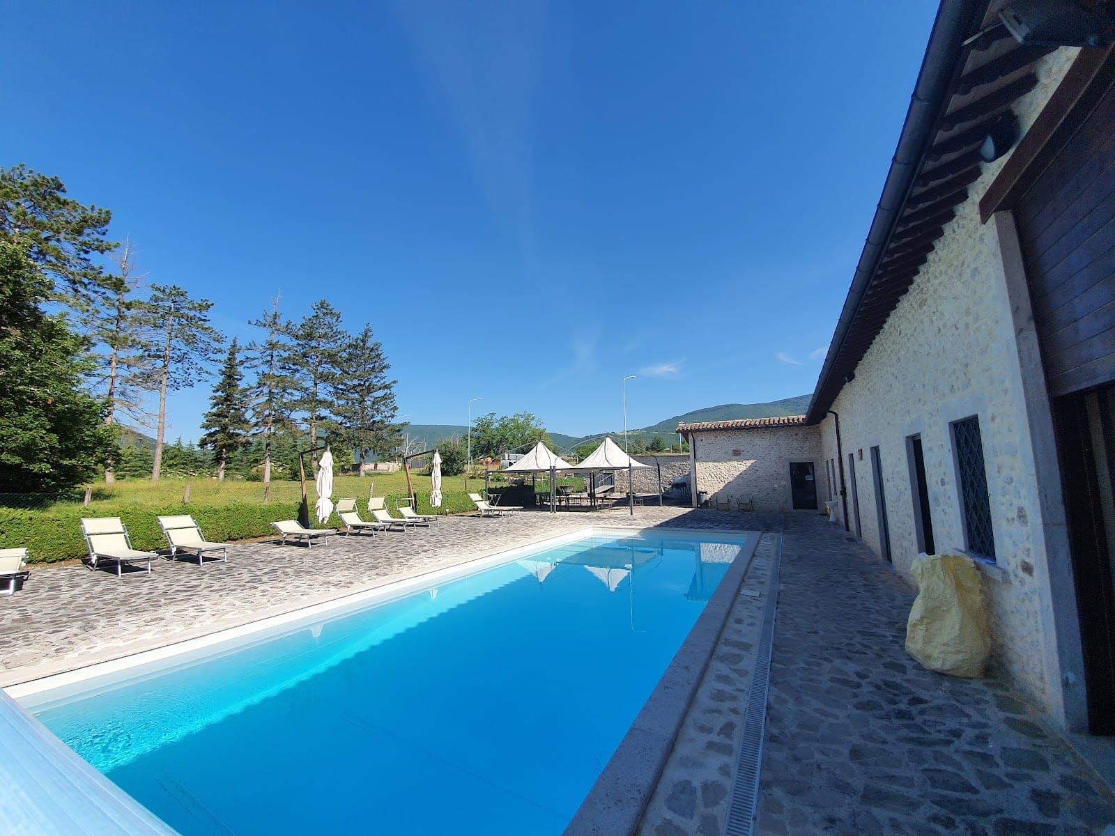 A swimming pool and lounge chairs are next to a stone building under a clear blue sky.