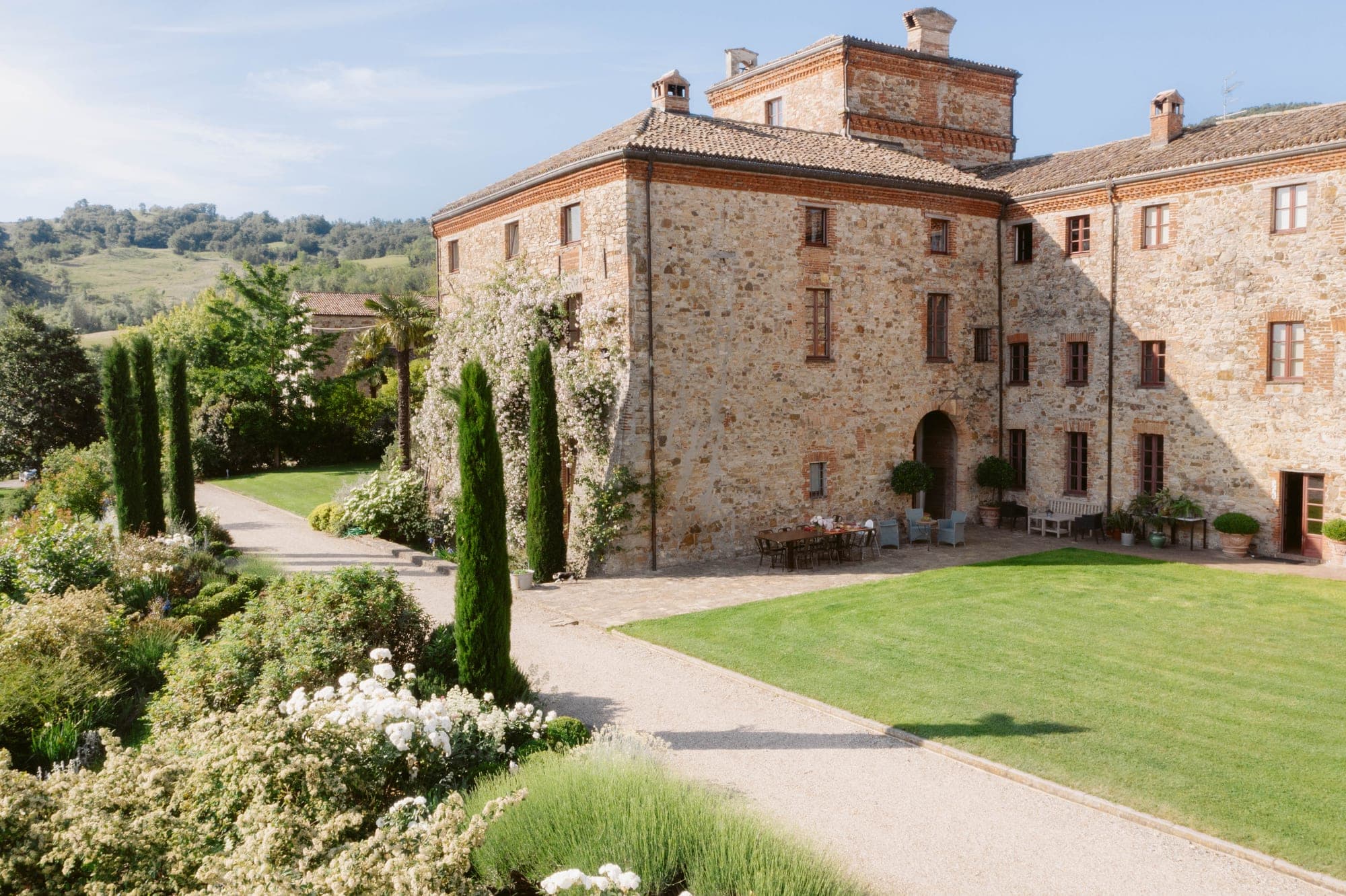 Courtyard of a stone building with gardens and cypress trees.