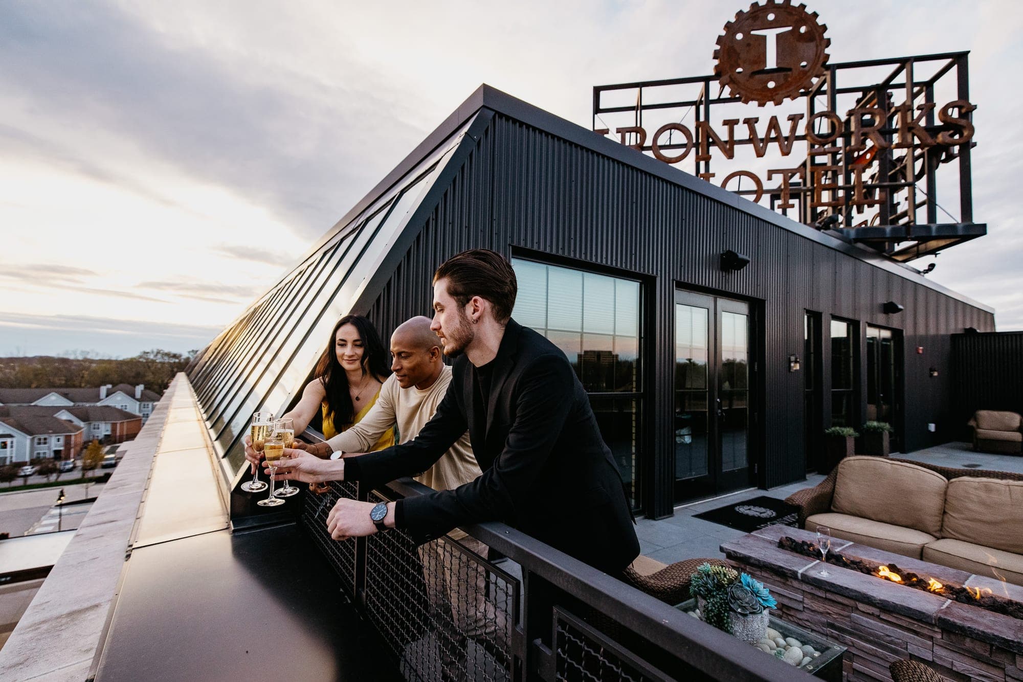People toasting on a rooftop terrace with a fire pit and seating.