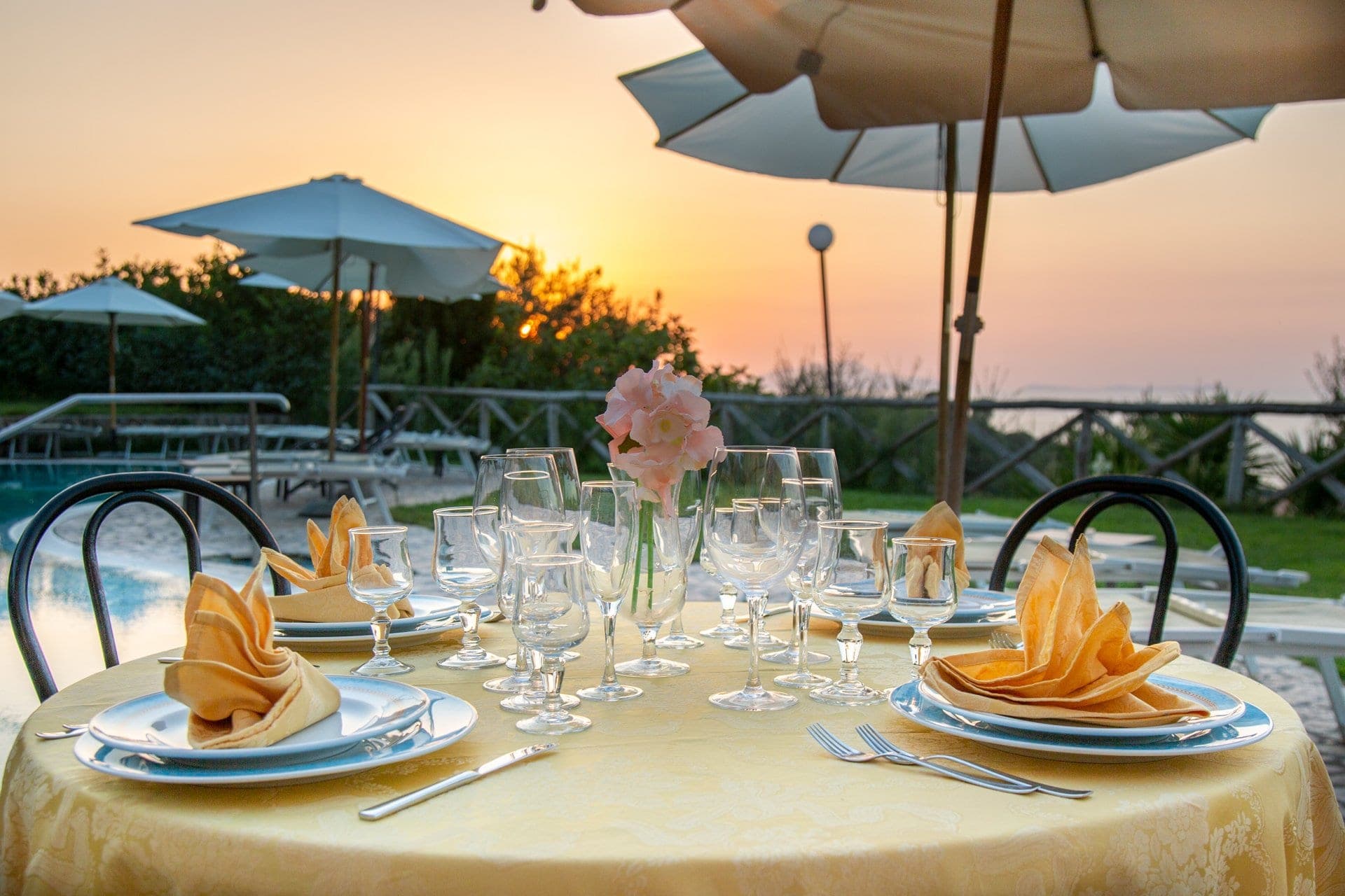 Outdoor dining table set with plates, glasses, and napkins at sunset.