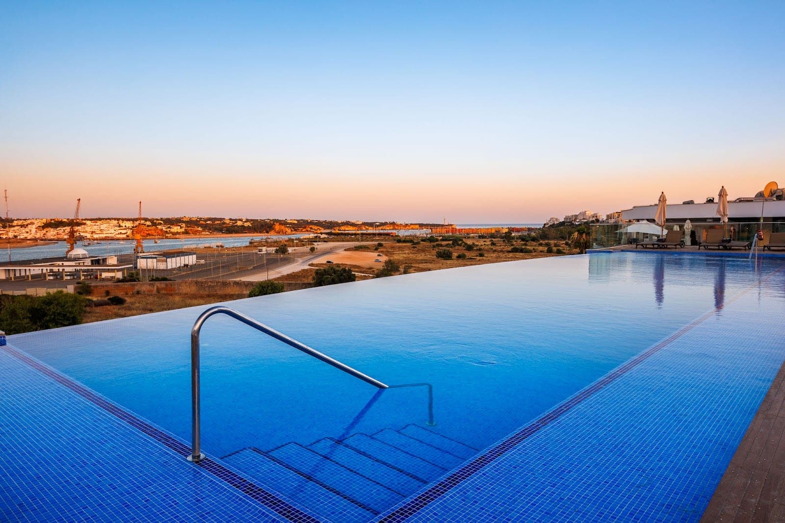 Infinity pool overlooking a marina and the sea at sunset.