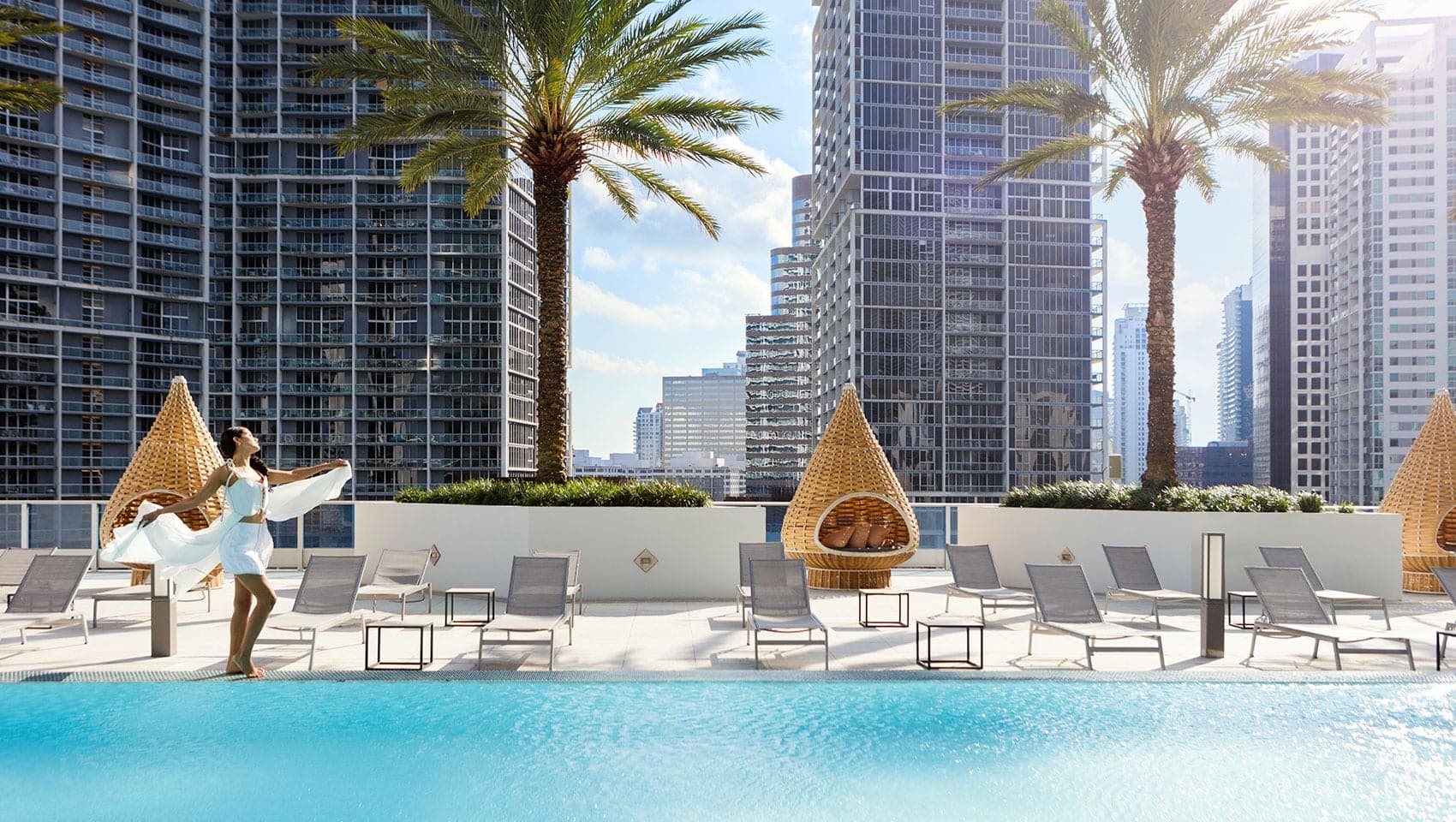 Woman by pool with palm trees and city skyline
