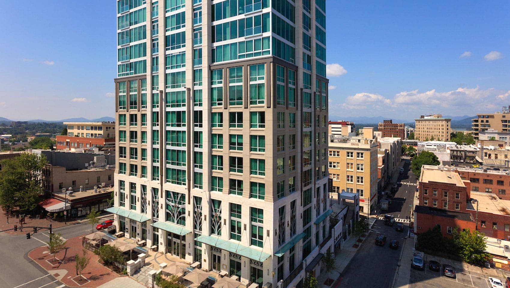 Exterior of a tall modern building in a city with mountains in the distance.