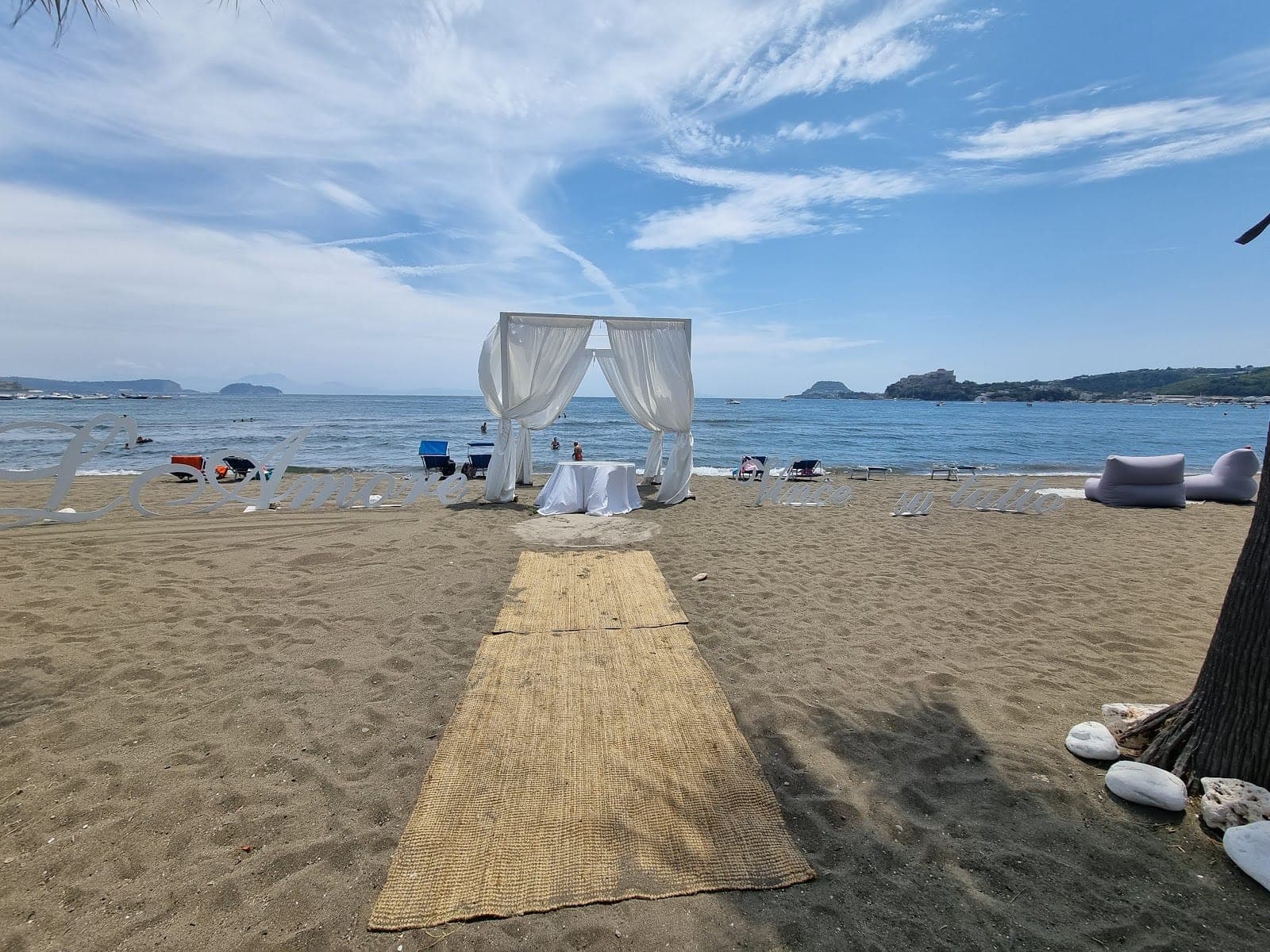 Beach ceremony setup with white canopy and aisle on sand overlooking the sea.