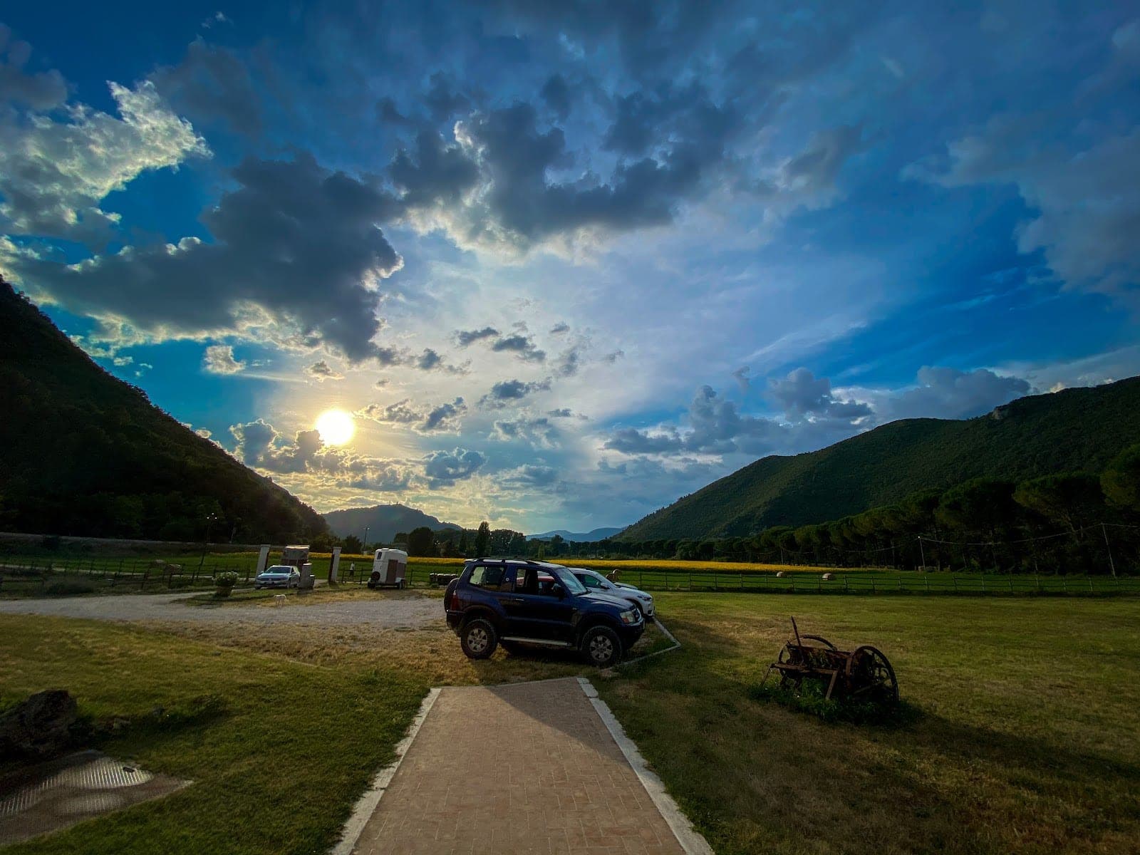Sunset over hills with cars parked in a grassy field.