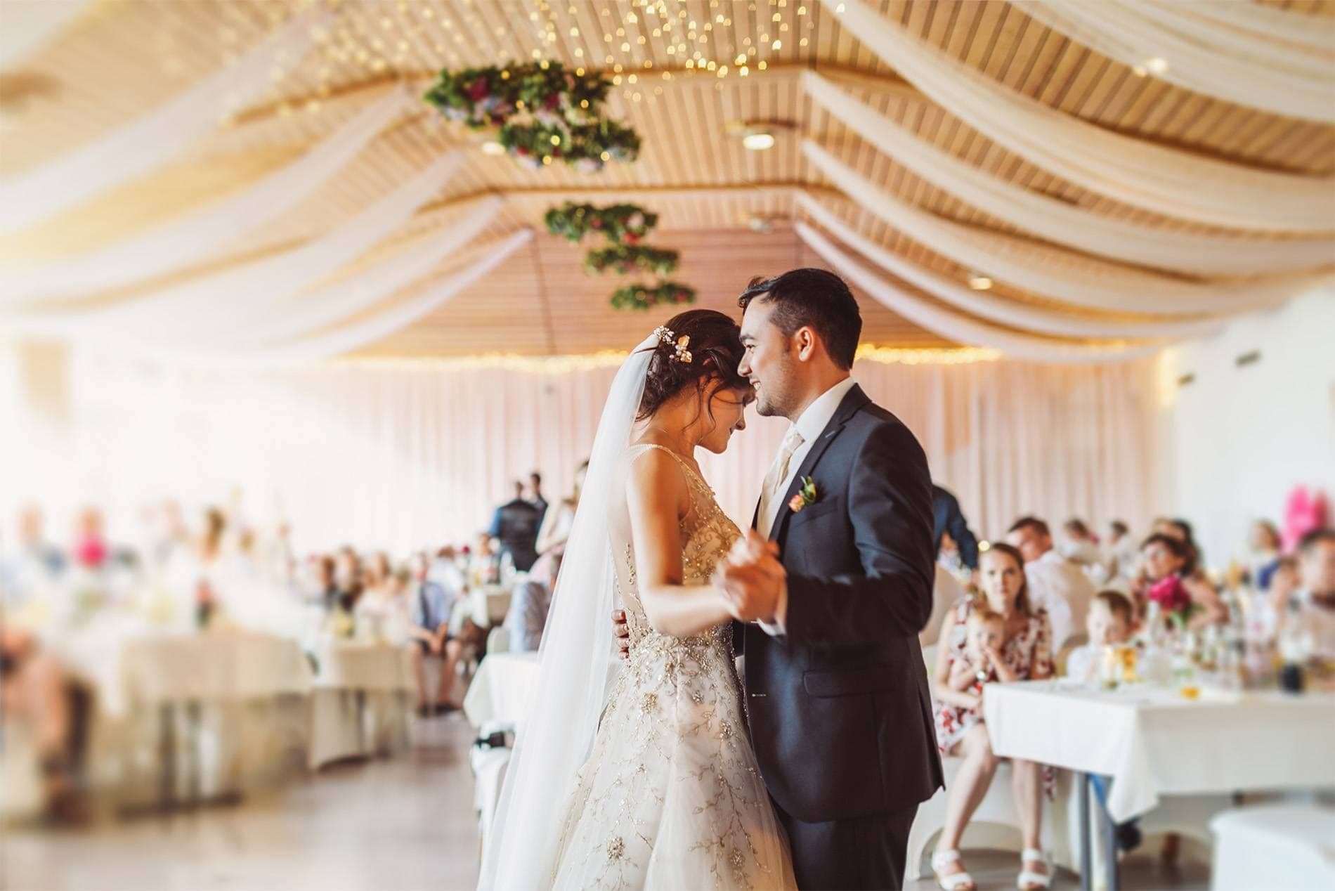 A bride and groom dance at their wedding reception in a decorated hall.