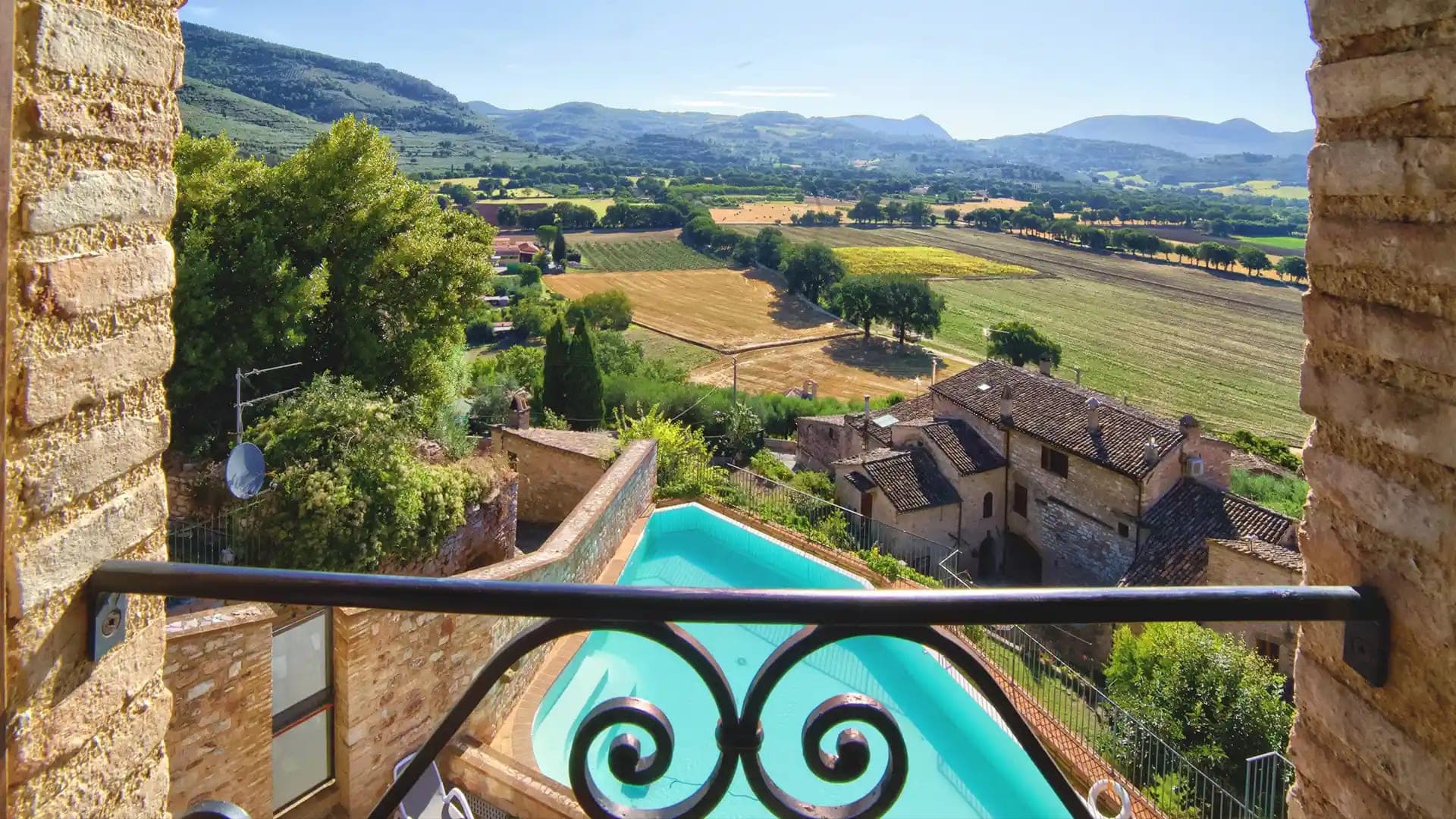 View of rolling hills and fields from a balcony with a swimming pool.