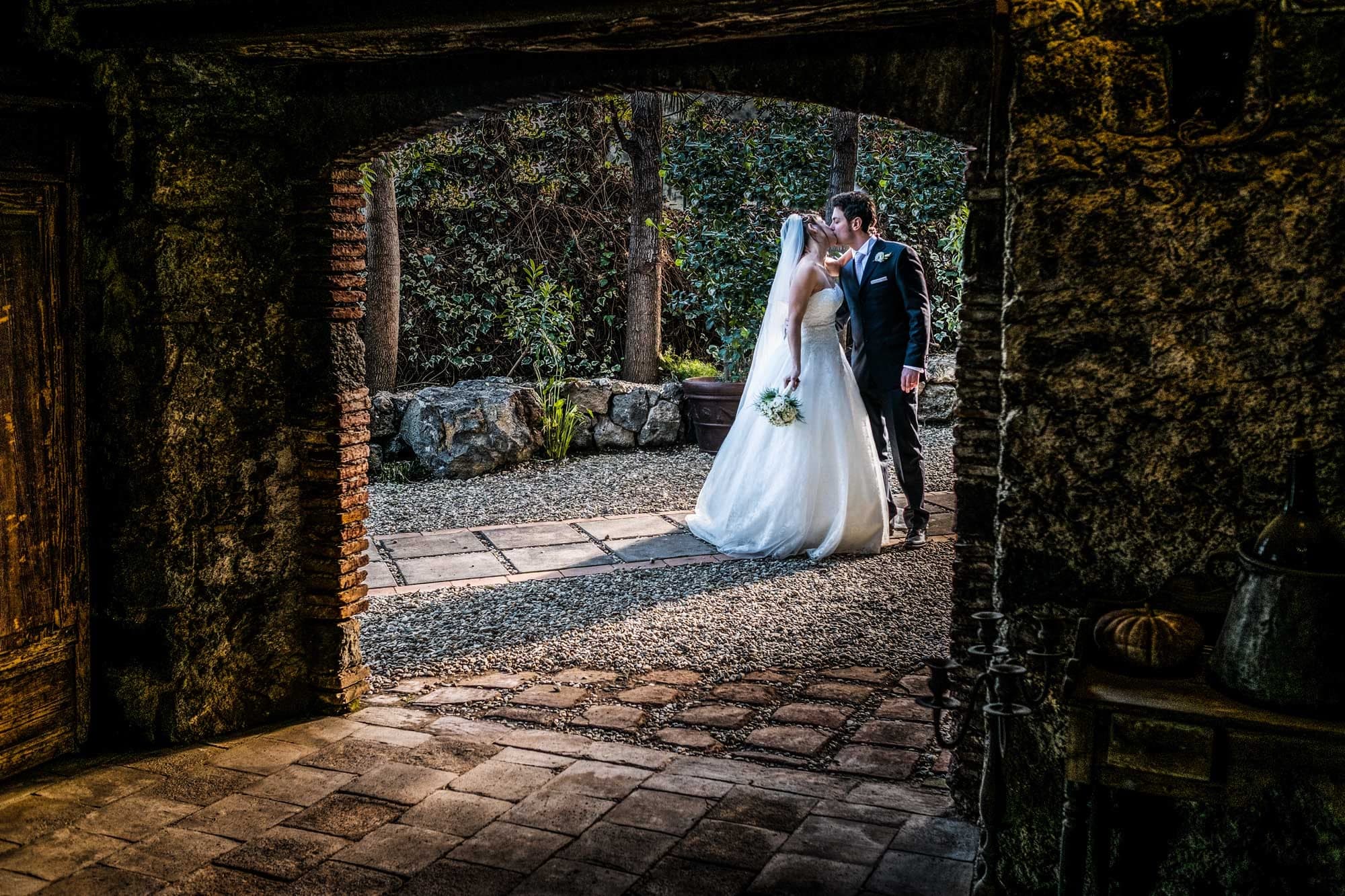 Bride and groom kissing in a garden courtyard.
