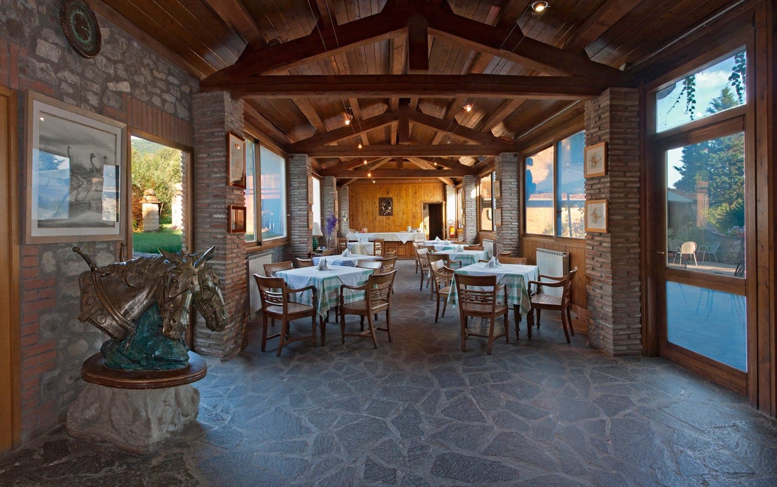 Dining room with tables set for a reception, large windows, and wooden ceiling.