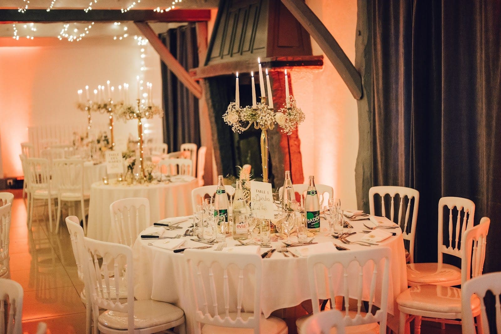 A wedding reception room with round tables set for dinner and lit by fairy lights.