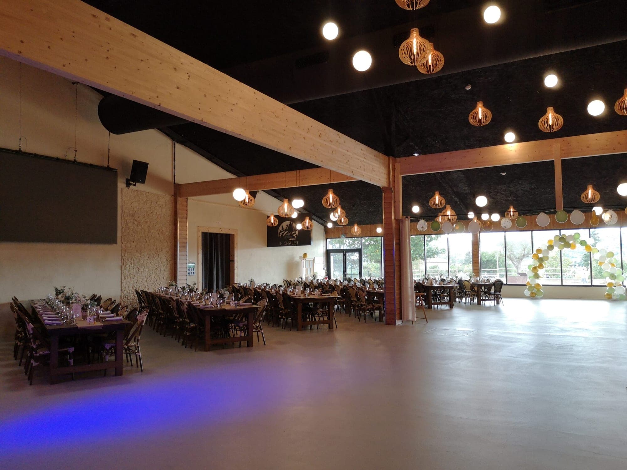 A large reception hall with tables set for a wedding and large windows.