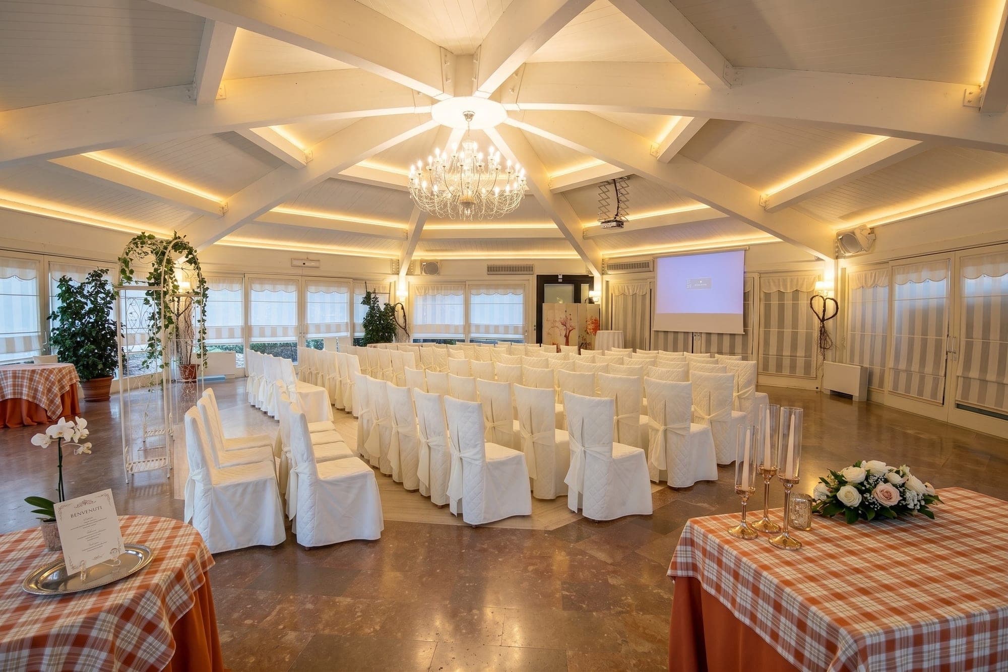 Indoor wedding ceremony setup with white chairs and an archway.