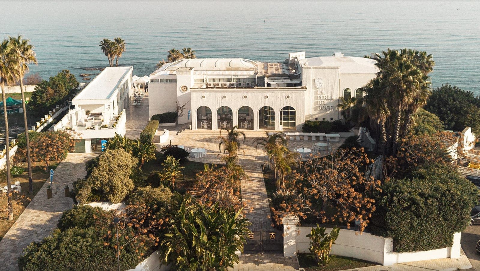 Aerial view of La Perla del Doge venue with palm trees and the sea.