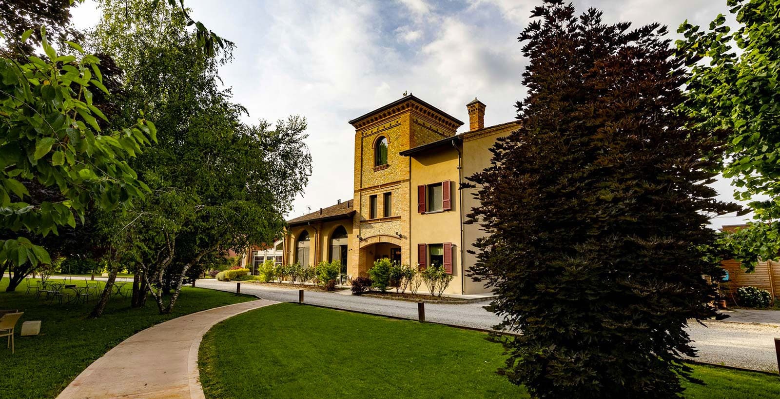 Exterior of a yellow building with a brick tower, surrounded by trees and a pathway.