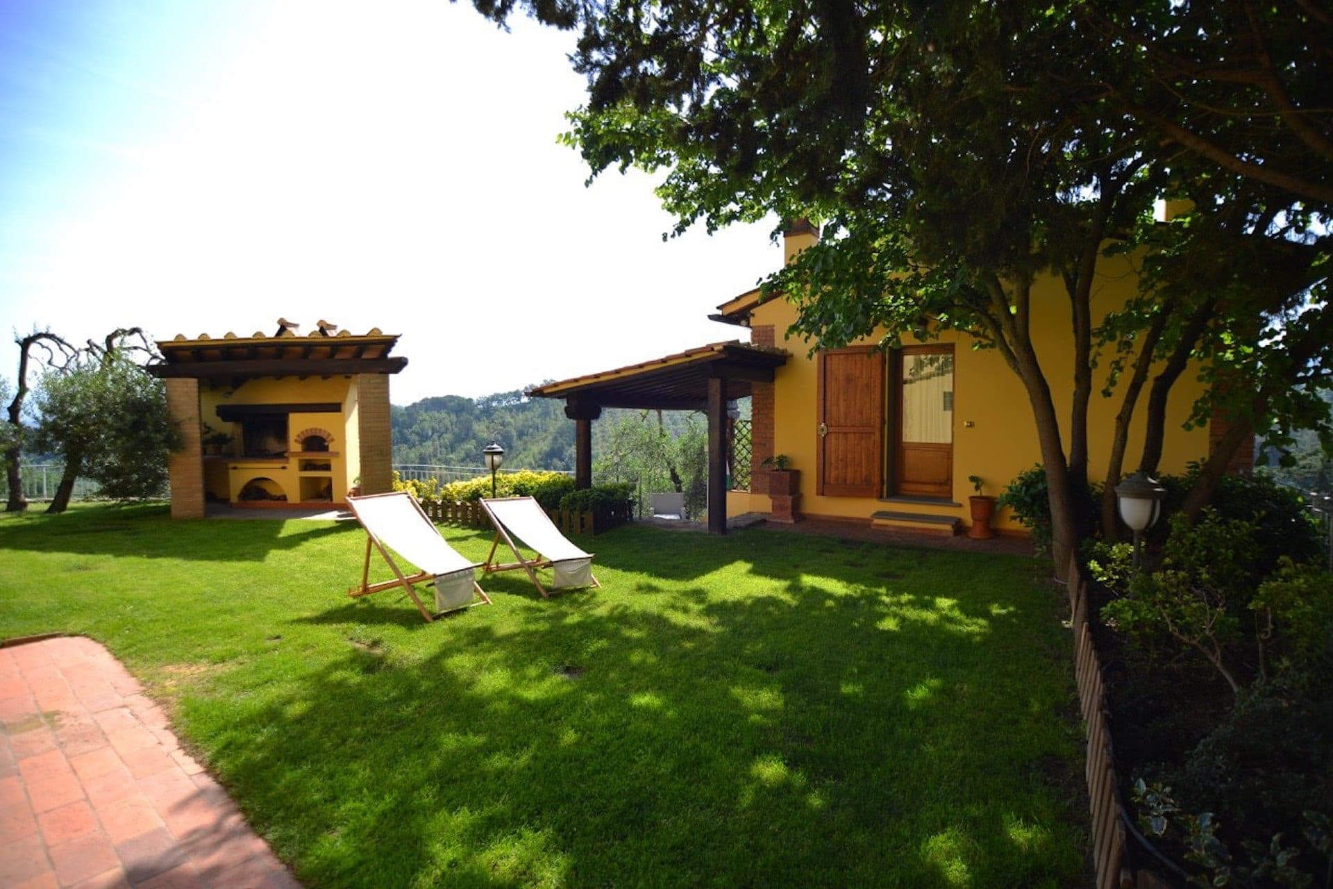 A sunny garden with two deck chairs and an outdoor pizza oven.