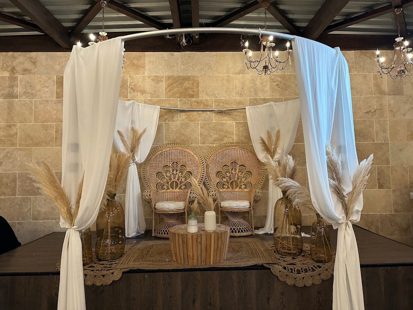 A decorated stage with two peacock chairs, pampas grass, and draped fabric.