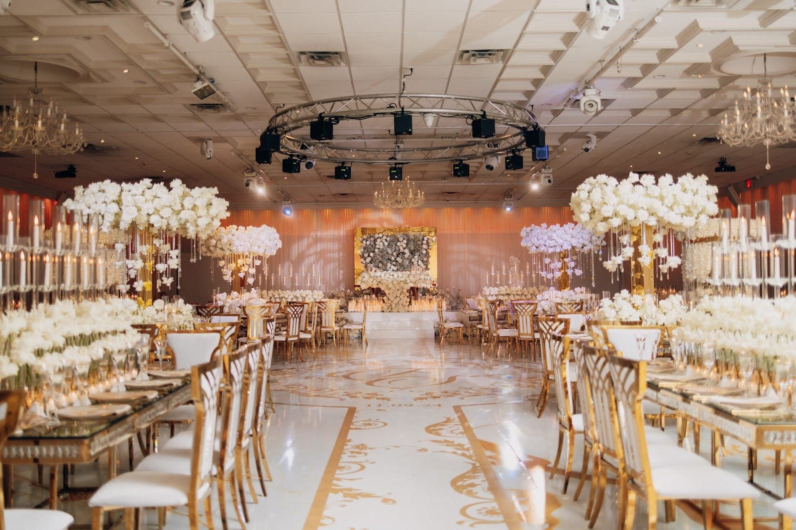 A grand ballroom set for a wedding reception with ornate floral arrangements and gold chairs.
