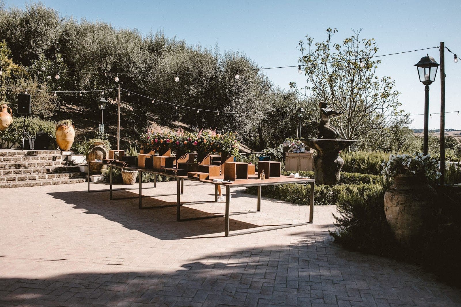 Outdoor terrace with tables and floral arrangements under string lights.