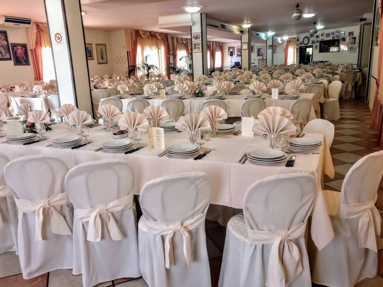 A reception room with tables set for a wedding, featuring white tablecloths and chairs.