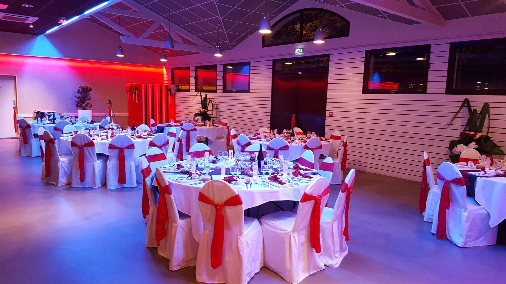 Wedding reception room with tables set for dinner and red and white chair decorations.