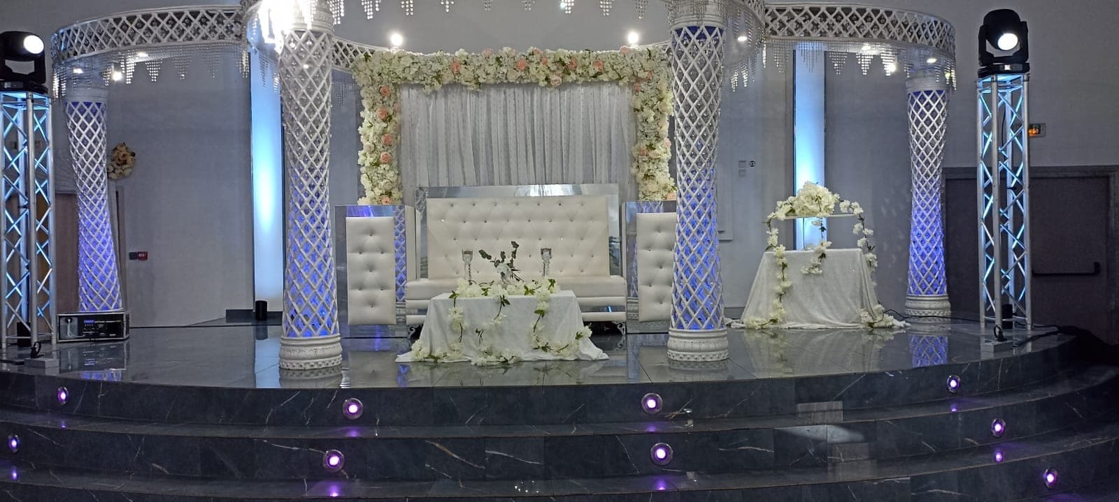 Decorated stage with white seating, tables, and floral arrangements.