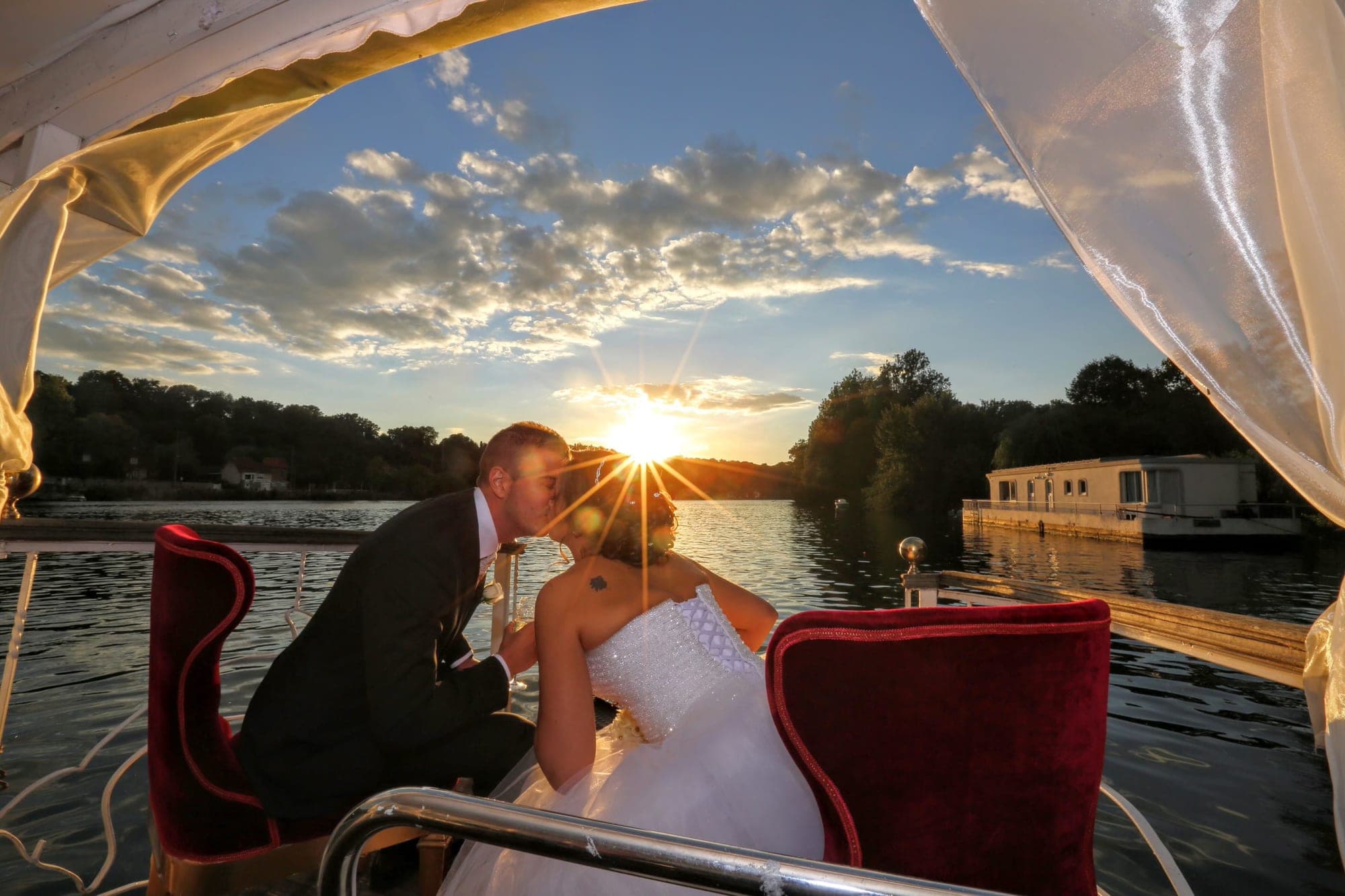Couple kissing on a boat at sunset with a houseboat in the background.