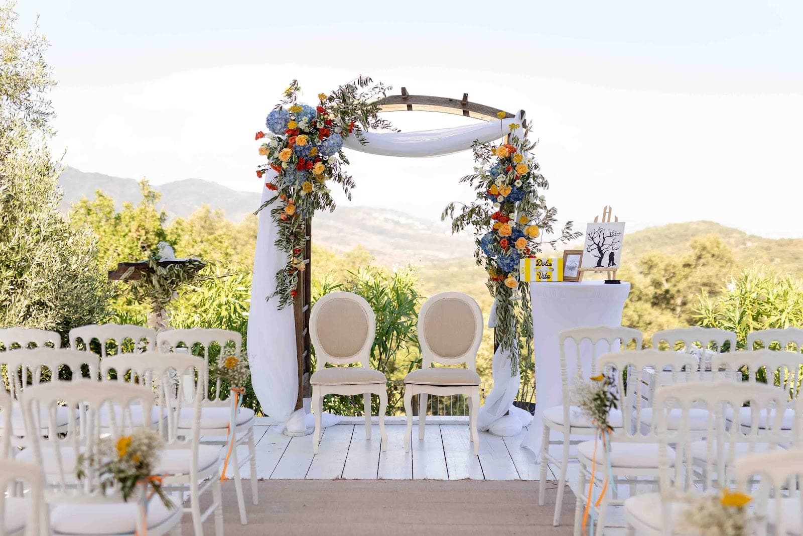 Wedding ceremony setup with chairs and floral arch outdoors with a scenic view.