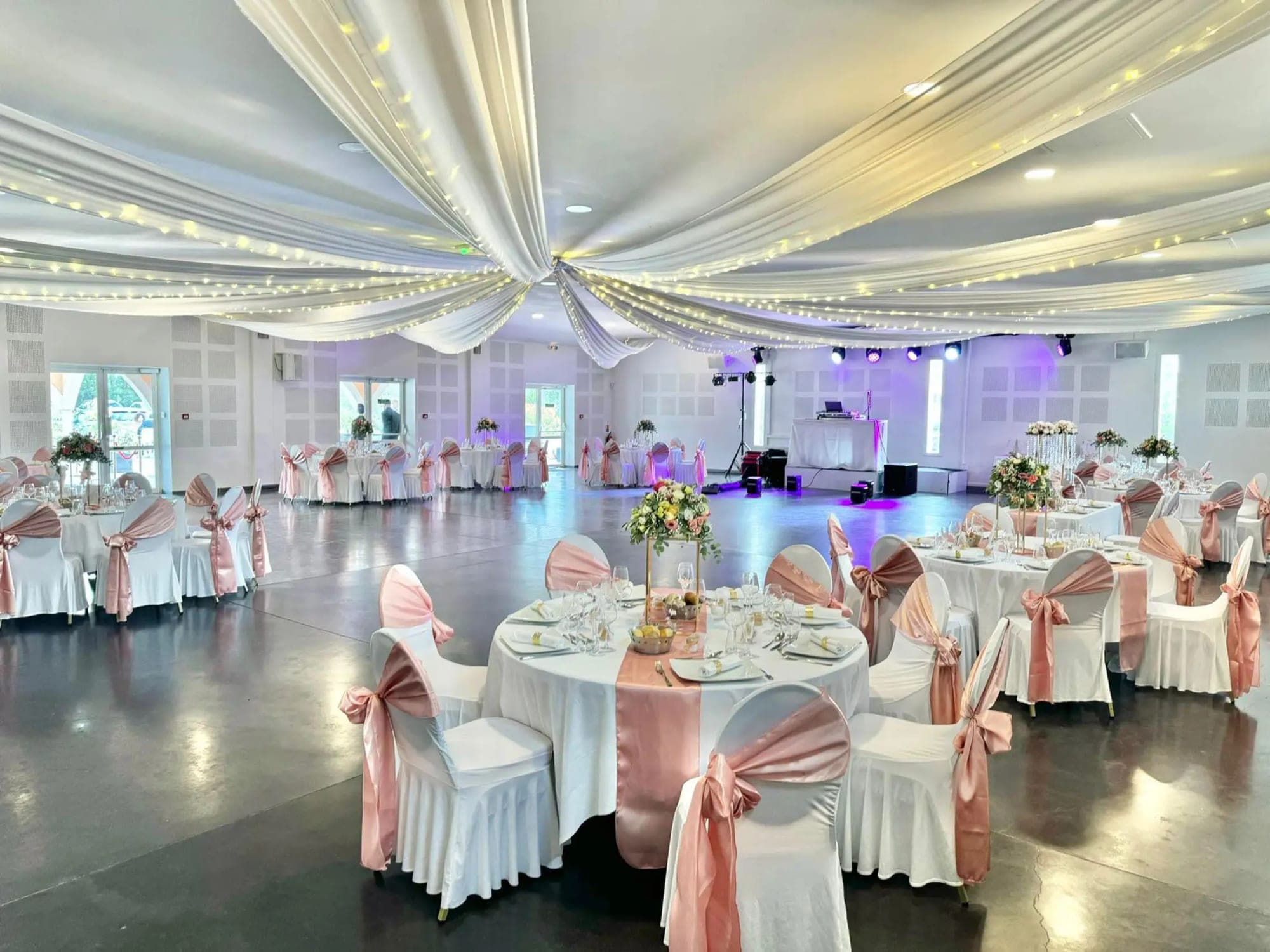Wedding reception hall with tables, chairs, and ceiling decorations.