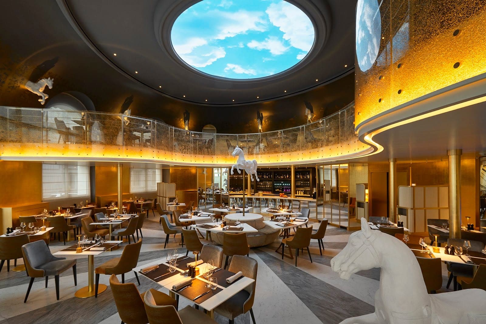 A circular dining room with a domed ceiling showing a sky, and horse sculptures.