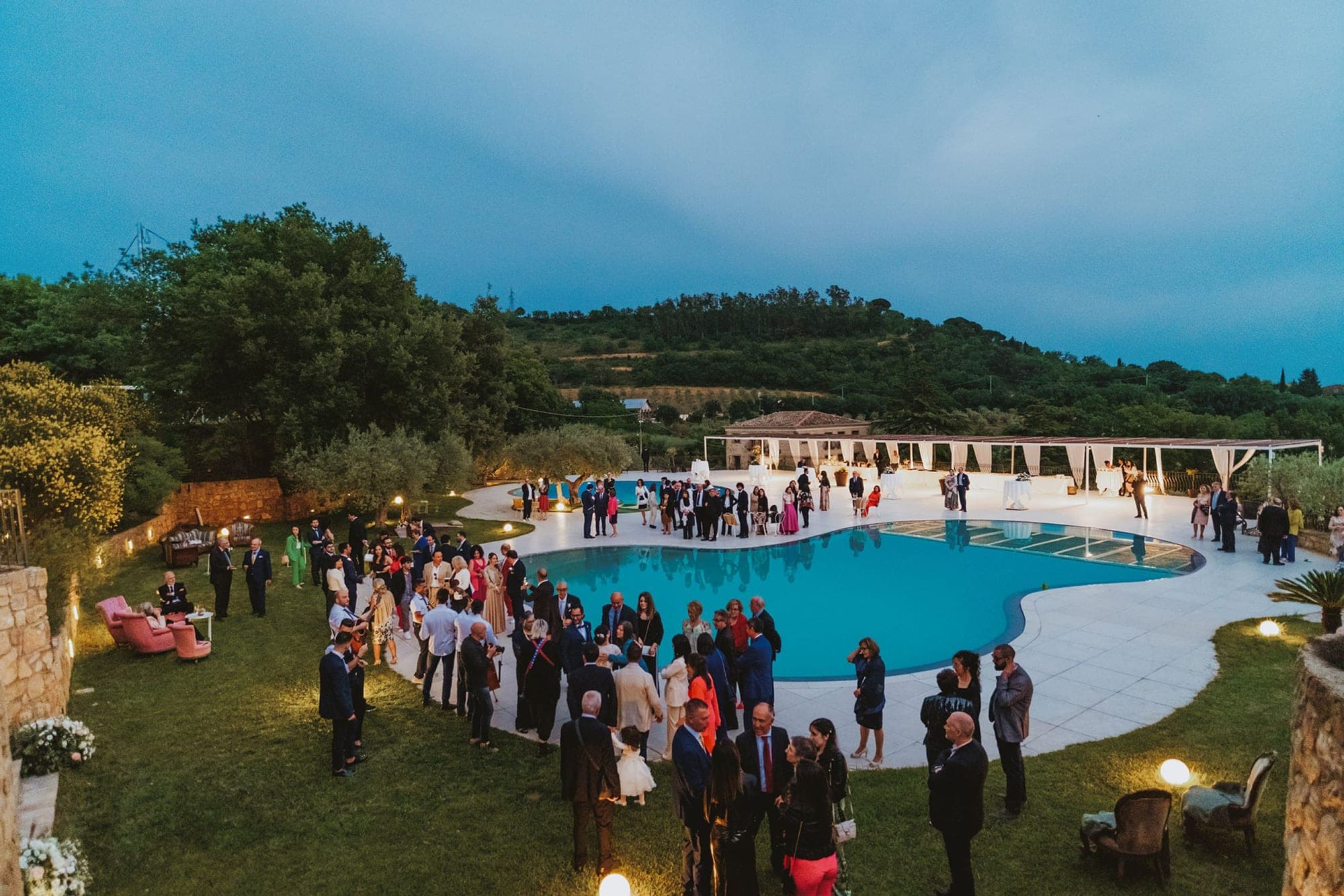 Wedding reception with guests around a pool and under white canopies.