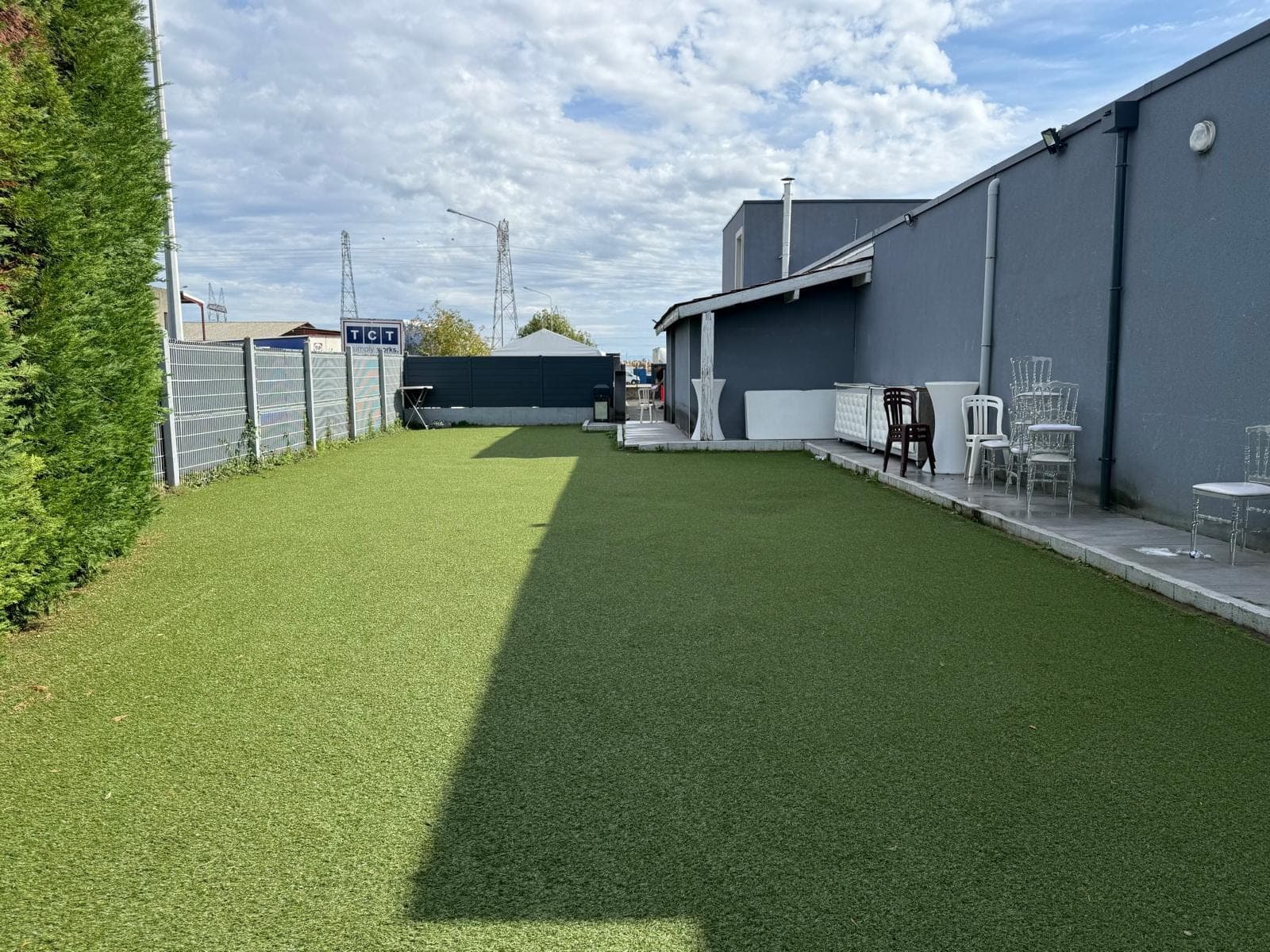 Outdoor area with artificial grass, chairs, and a building.