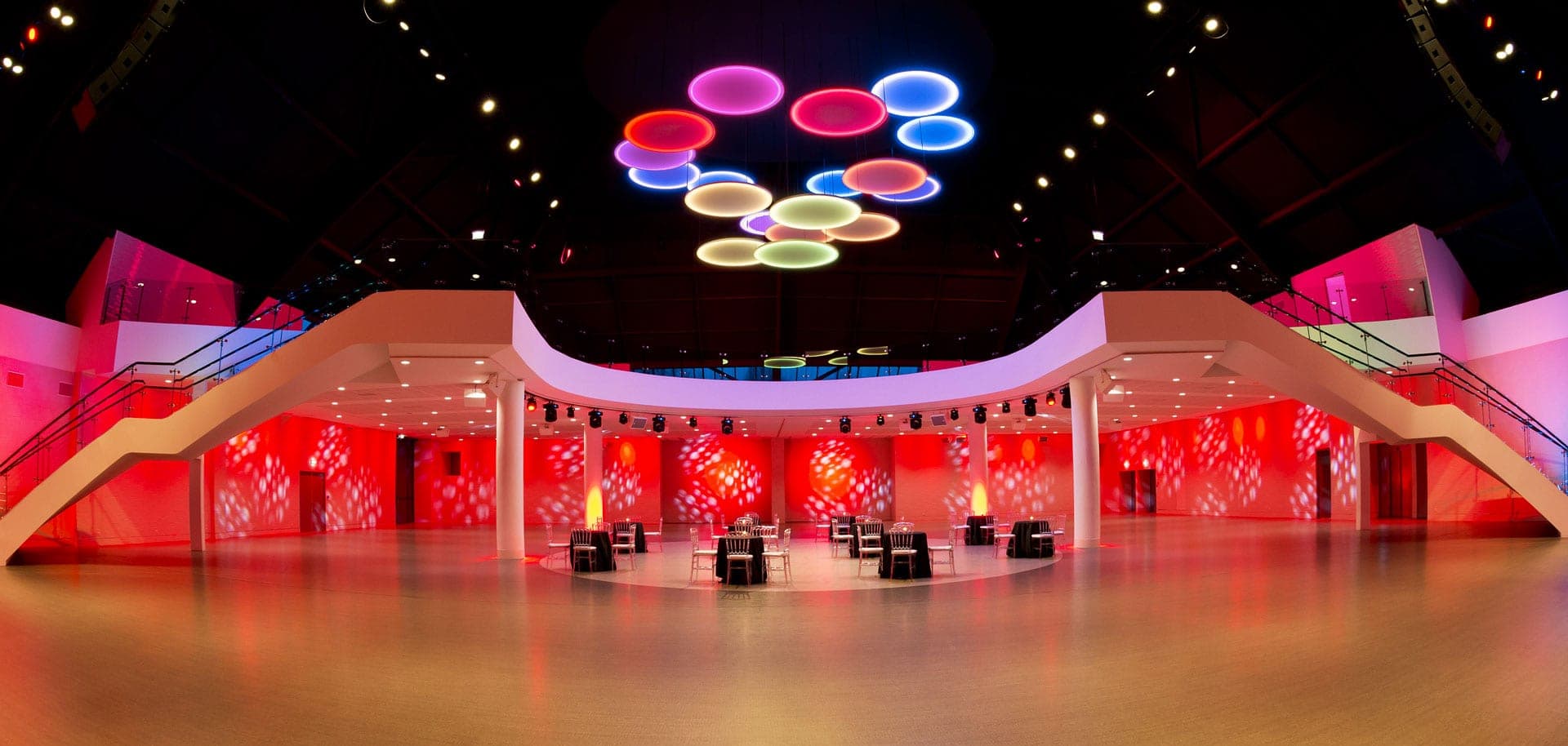 A wide view of a modern event hall with red lighting and tables set for a reception.