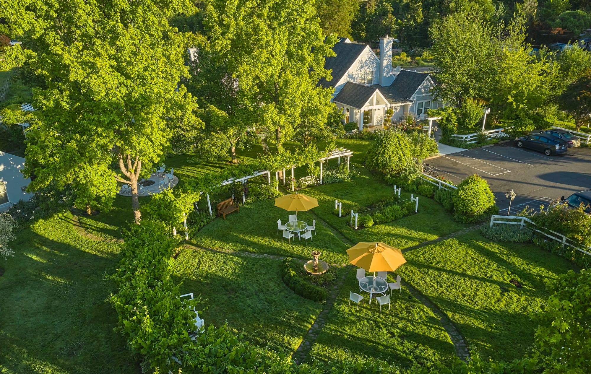 Aerial view of a garden with tables and umbrellas, and buildings in the background.