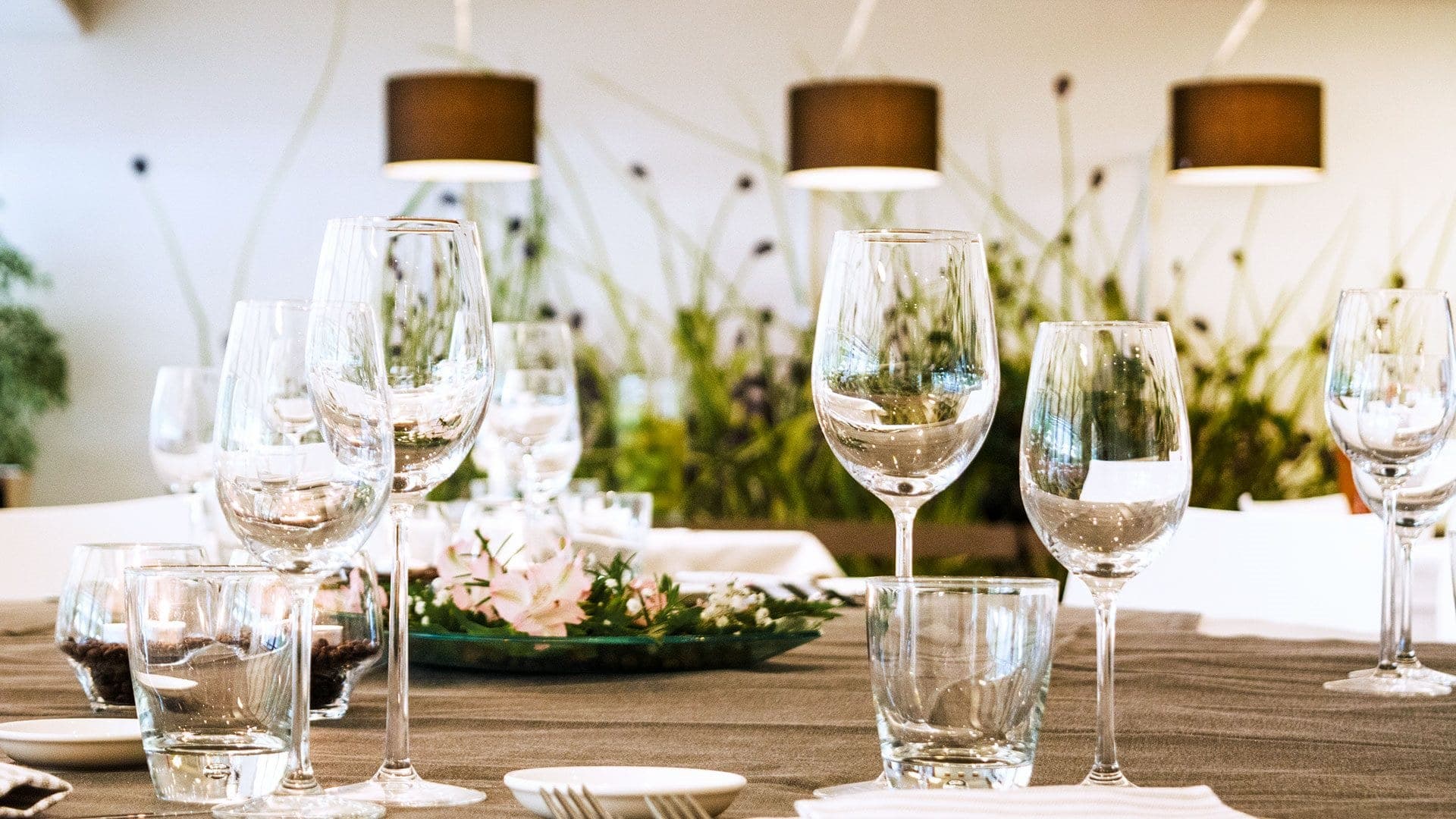 A table set for a reception with wine glasses and a floral arrangement.