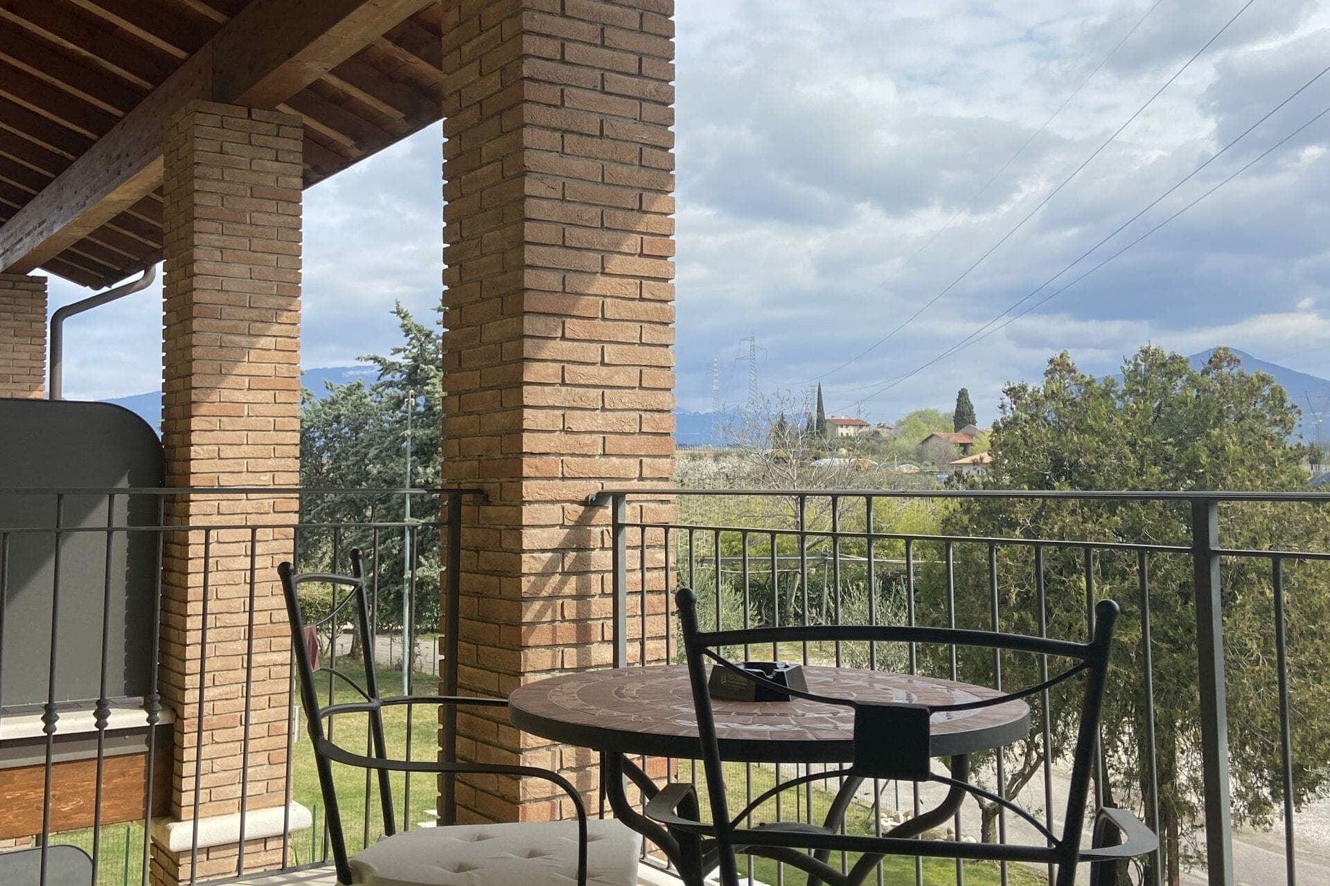 Balcony with table and chairs overlooking a landscape with hills and trees.