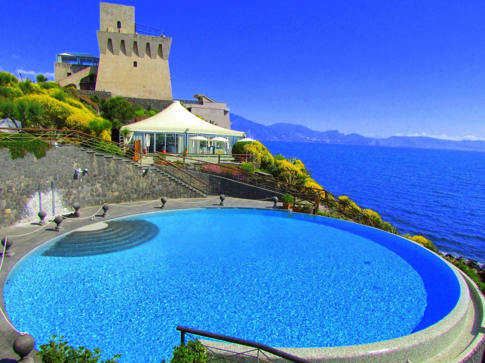A swimming pool and a tower by the sea on a sunny day.