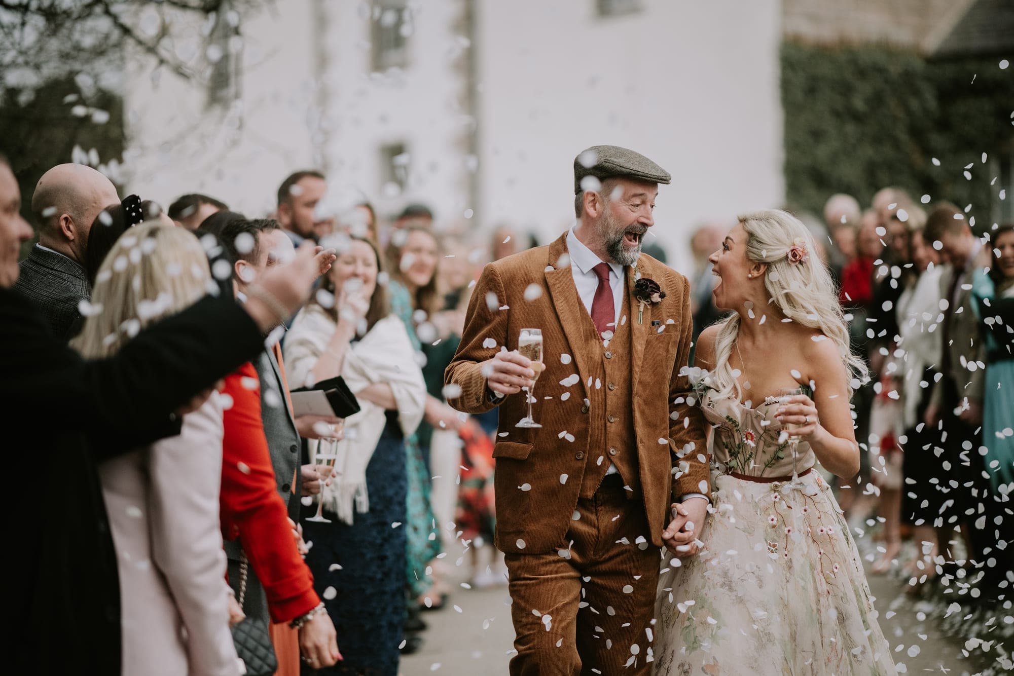 A bride and groom walk through confetti with guests at a wedding.