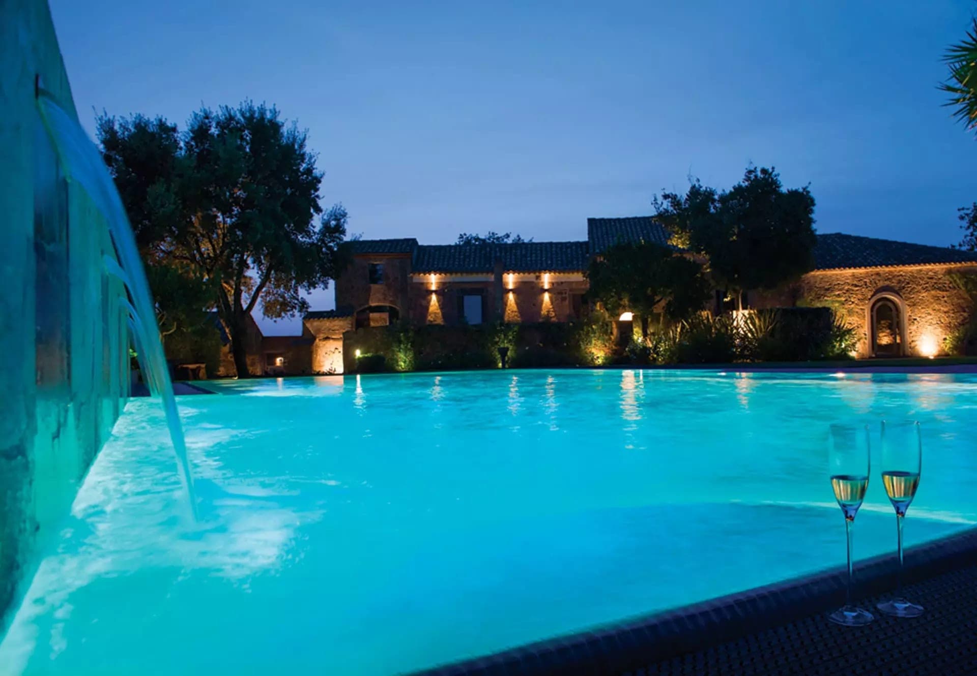 Swimming pool and building at night with two glasses of champagne