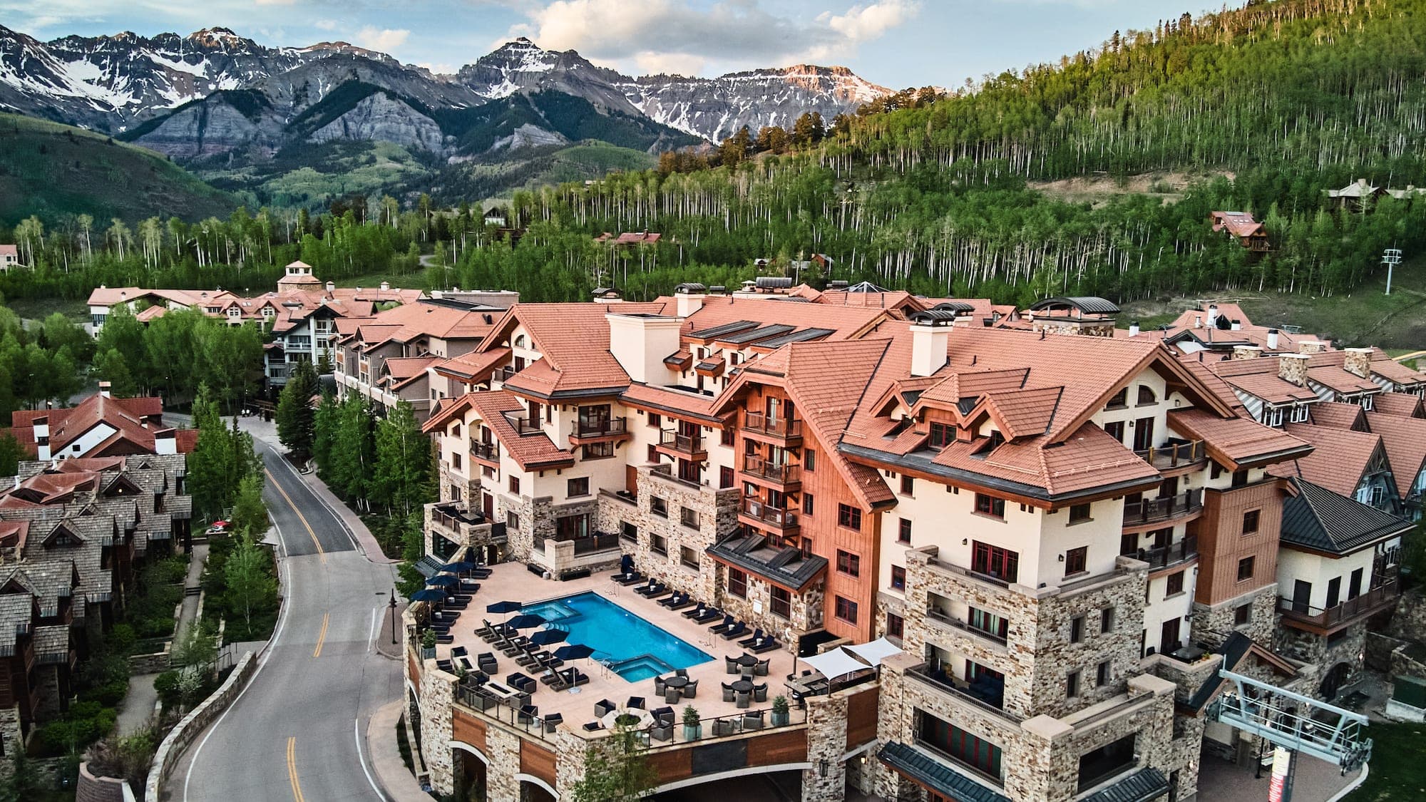 Aerial view of a resort complex with a pool and mountains in the background.