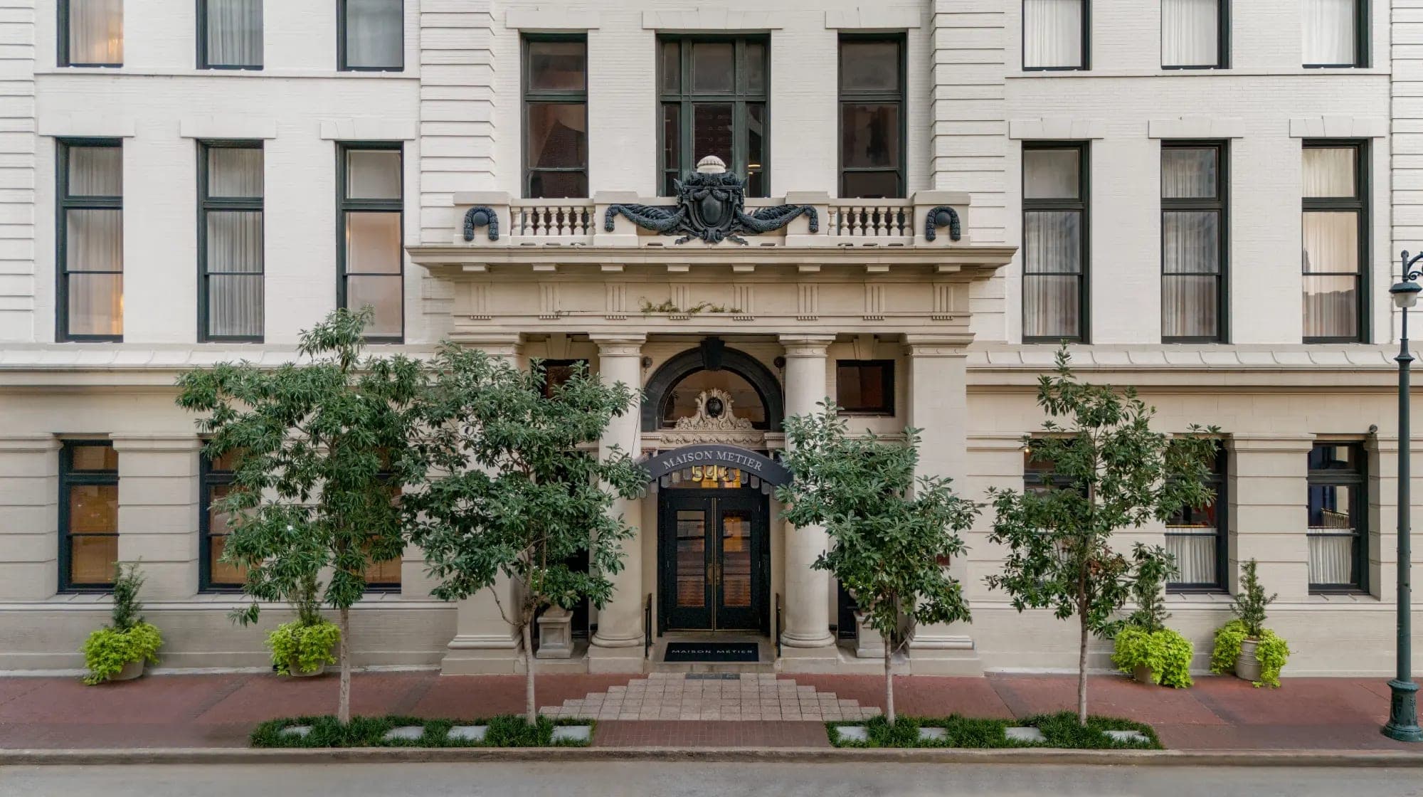 Exterior of Maison Metier building with an arched entrance and trees.