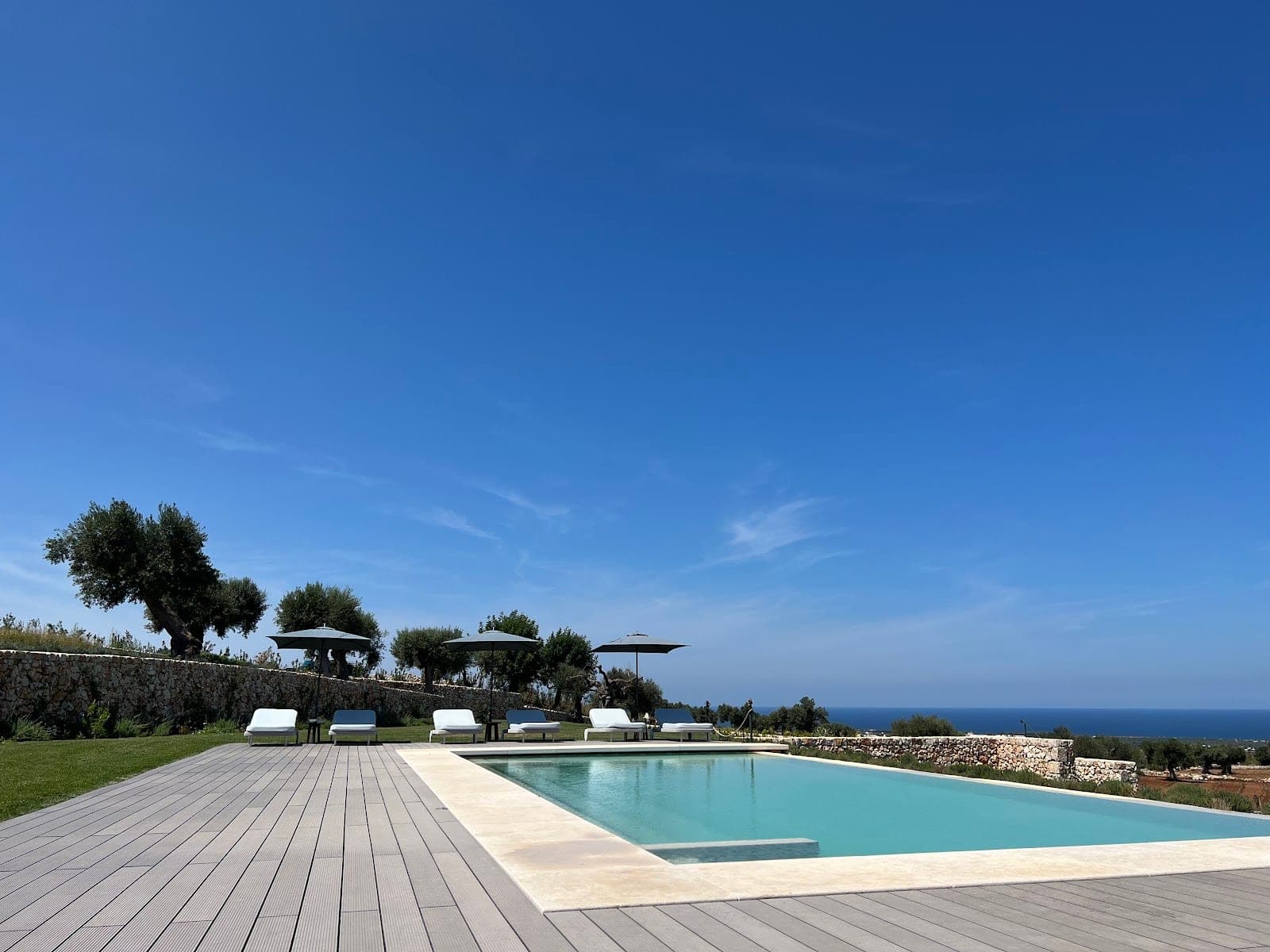 Swimming pool and lounge chairs with a view of the sea under a clear blue sky.