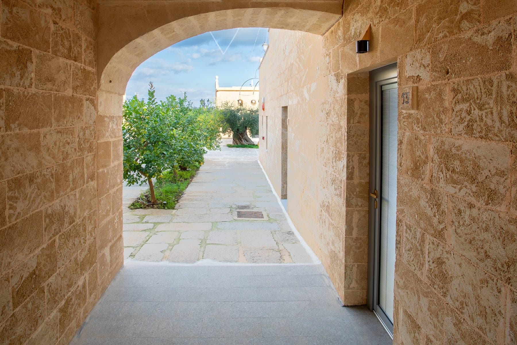 Pathway through an archway with trees and buildings in the background.