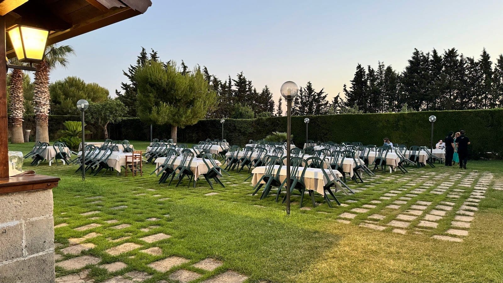 Tables and chairs set up on a lawn at dusk with trees in the background.