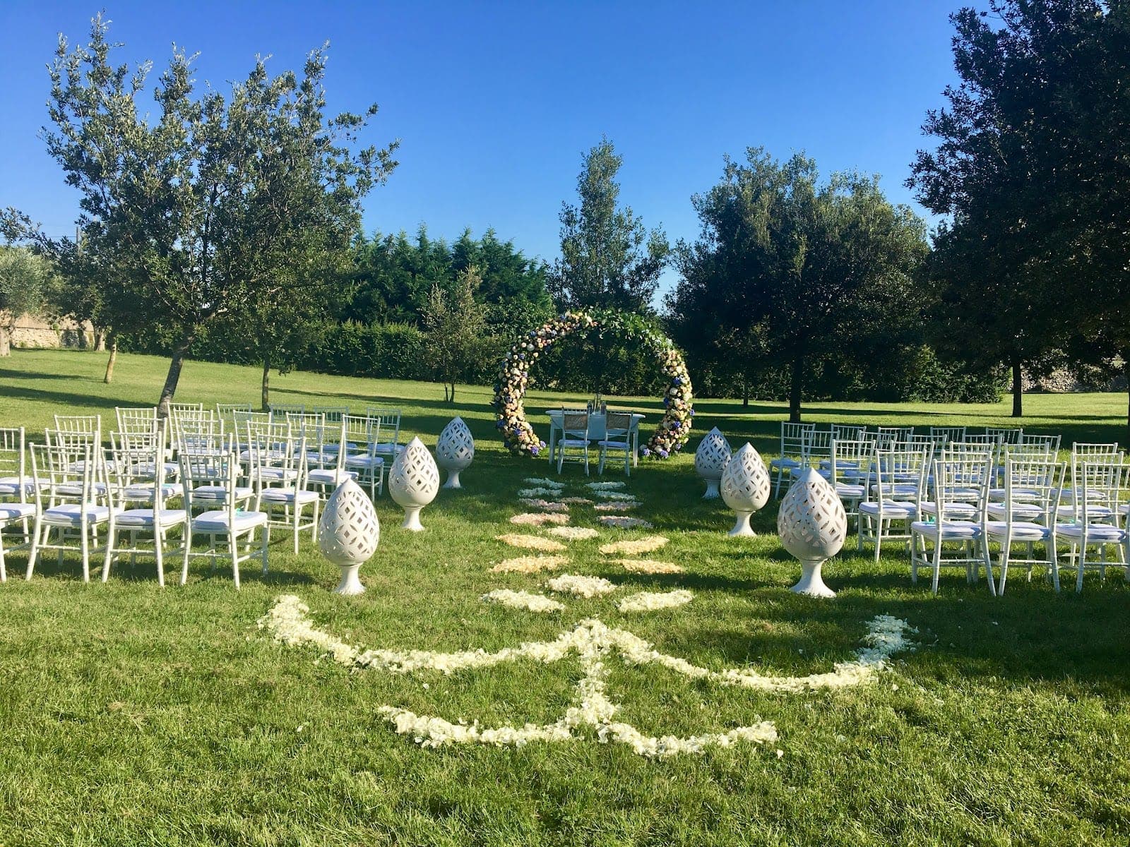 Wedding ceremony setup in a garden with chairs and a floral arch.