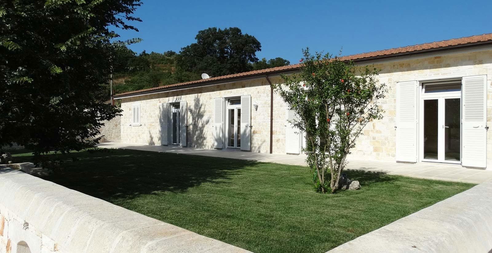 Exterior of a stone building with white shutters and a green lawn.