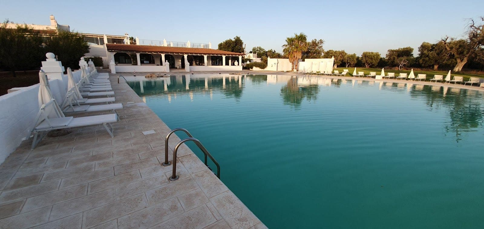 A large swimming pool with lounge chairs and a building in the background.